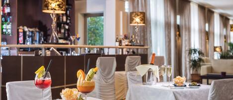 A restaurant with a bar area, tables with white tablecloths, and a variety of drinks and snacks.