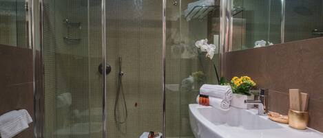 Ein modernes Badezimmer mit einer begehbaren Glasdusche, einem weißen Waschbecken und einem Waschtisch mit Pflegeprodukten.