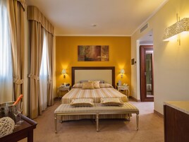 Habitación de hotel con una cama grande, dos mesitas de noche, un banco y vistas al baño.