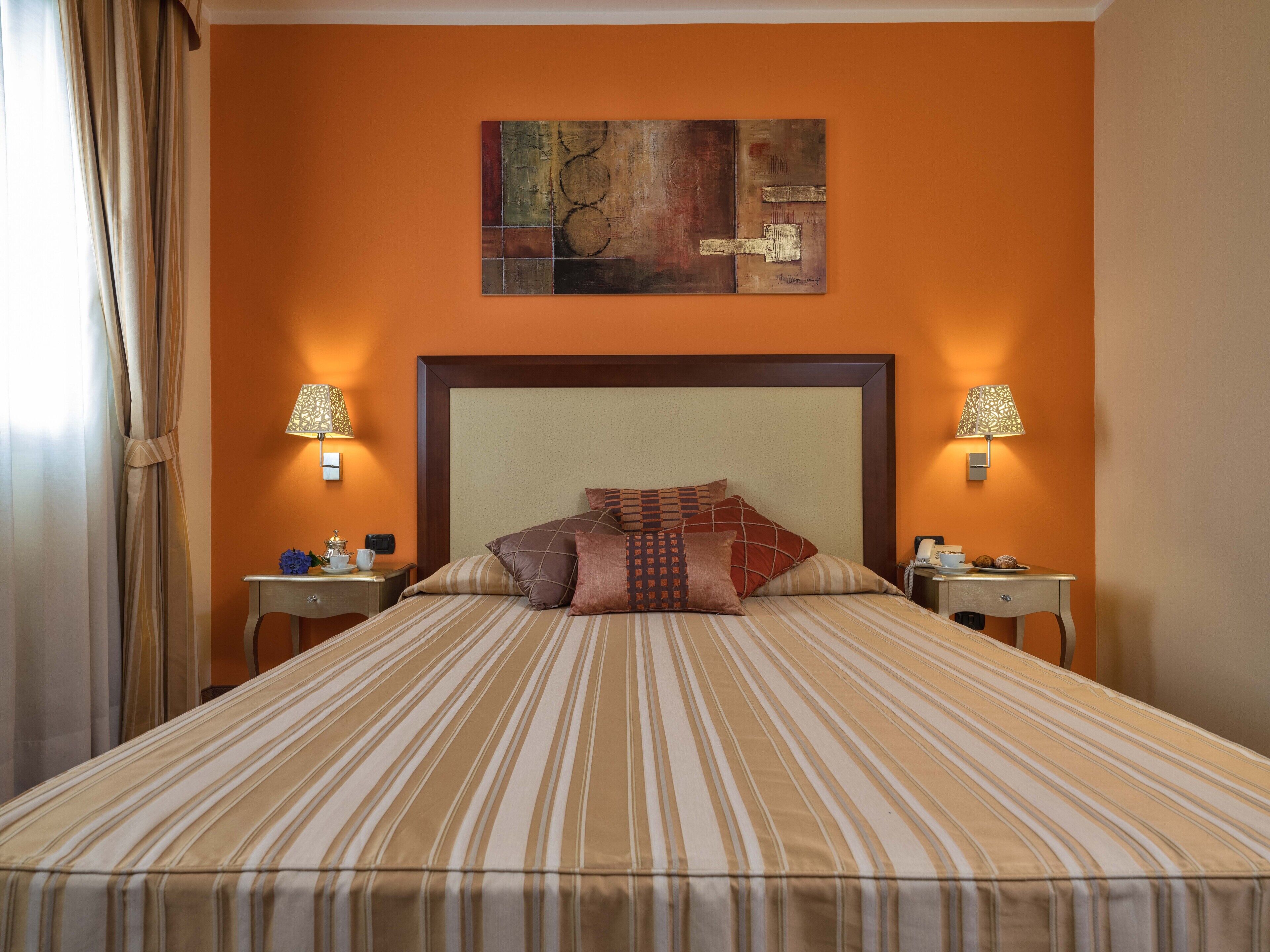 A hotel room with a large bed, two bedside lamps, a nightstand, and a painting on the wall.