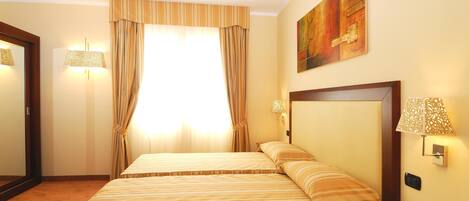 Quarto de hotel com duas camas, uma janela grande com cortinas, um quadro na parede e um telefone ao lado da cama.