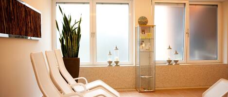 A waiting area with reclining chairs, a potted plant, a glass cabinet with candles, and a clock on the wall.