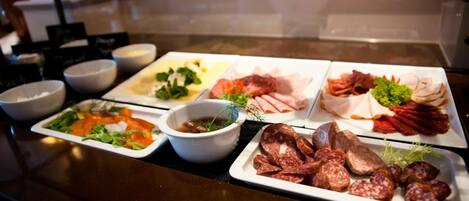 Un bufé con diversos platos, incluyendo carnes, quesos y ensaladas.