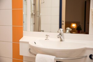 Un baño con un lavamanos blanco, un espejo grande y azulejos naranja en la pared.