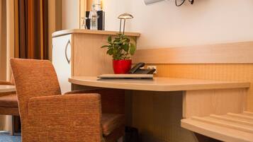 Een hotelkamer met een houten bureau, een rode plant, een lamp, een telefoon en een aan de muur bevestigde televisie.
