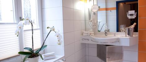 Un baño moderno con ventana, orquídeas en macetas, lavamanos y espejo.