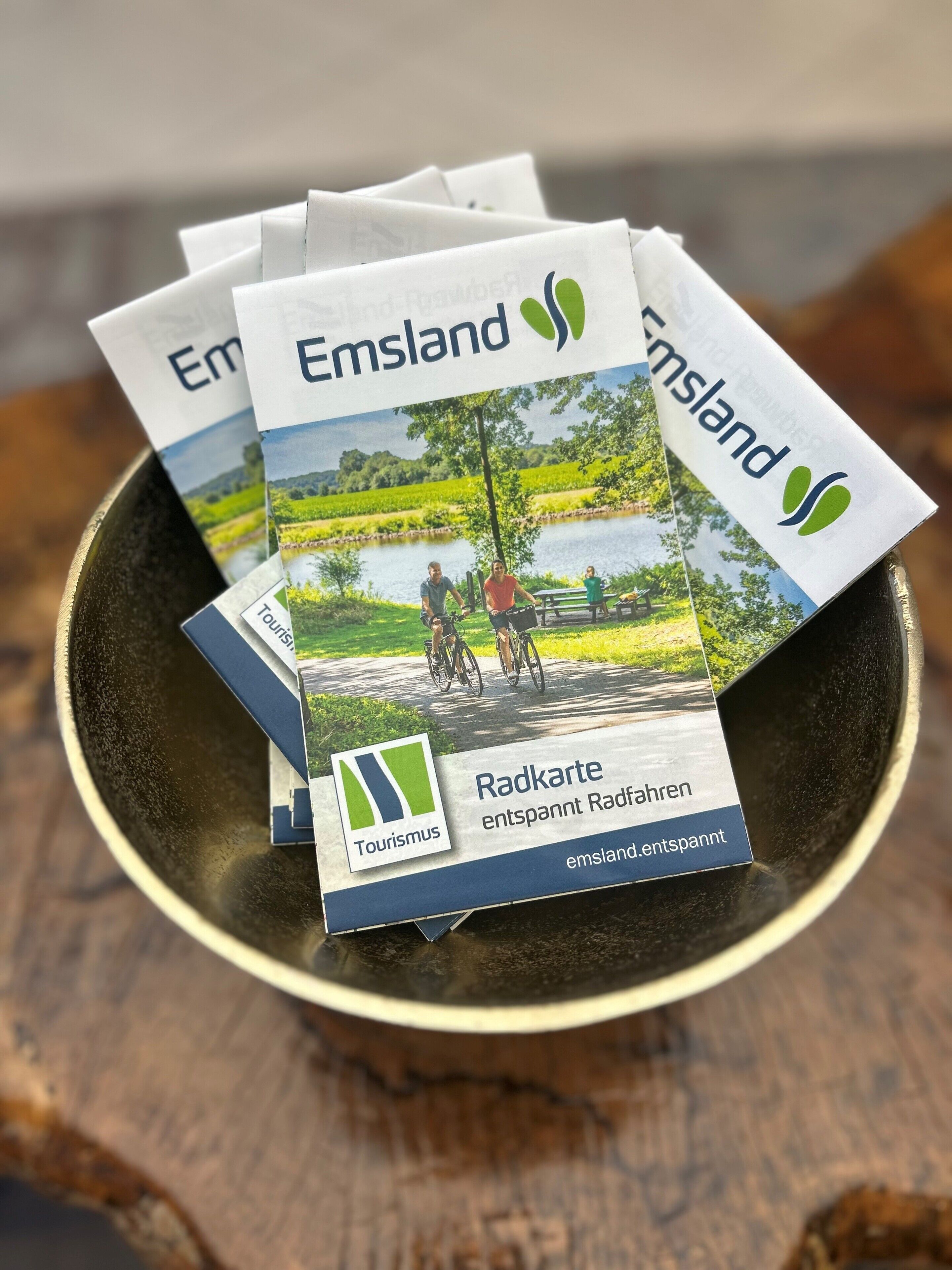 Un récipient contenant des dépliants arborant la marque « Emsland » et le logo « Tourismus », indiquant qu’il s’agit de documents d’information touristique.