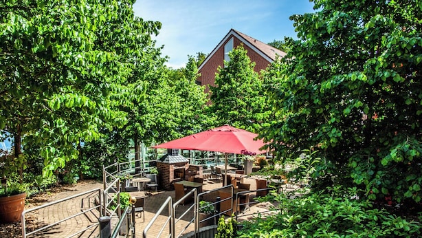 A patio area with outdoor seating, a brick oven, and a red umbrella. - Hotel von Euch (Meppen)