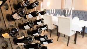 A wine rack with multiple bottles in a dining area with white chairs and a table. - Hotel von Euch (Meppen)