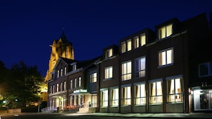A hotel with a traditional facade, multiple windows, and a prominent tower in the background. - Hotel von Euch (Meppen)