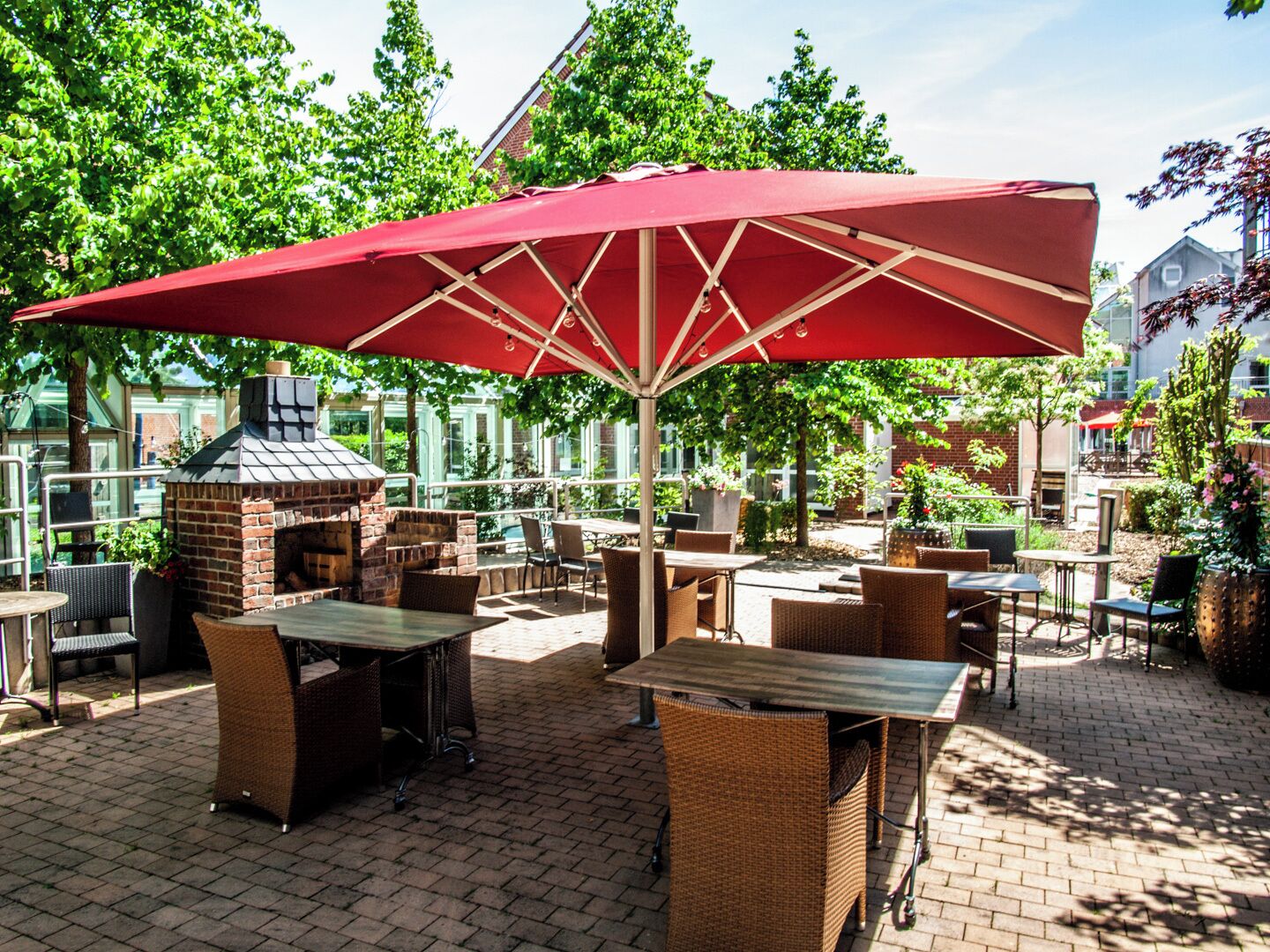 Eine Terrasse im Freien mit Korbmöbeln, einem Kamin aus Ziegelsteinen und einem roten Sonnenschirm.