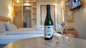 A hotel room with a bed, a bottle of Meppen Perlen wine, and a wine glass on a table. - Hotel von Euch (Meppen)
