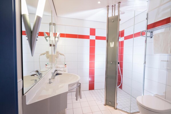 A modern bathroom with a large mirror, two sinks, a glass shower enclosure, and a toilet.