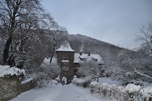 A snow-covered building with a stone facade and a central tower, surrounded by snow-laden trees and a hill in the background. - Schaumburger Ritter Hotel & Restaurant (Rinteln)