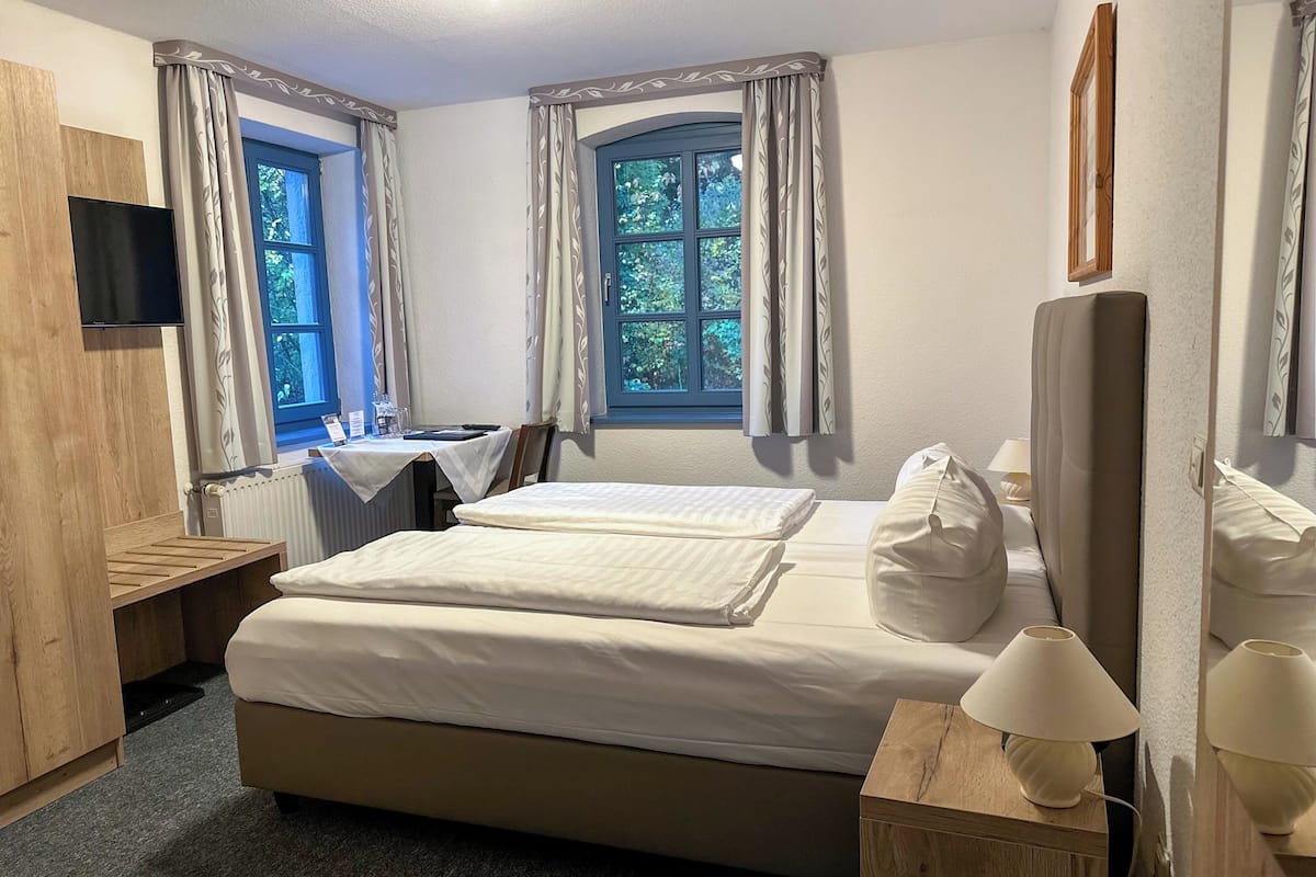 A hotel room with a bed, bedside tables, a desk, a chair, a TV, and a window with curtains.