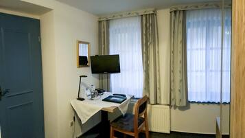 A hotel room with a desk, chair, television, and windows with curtains.