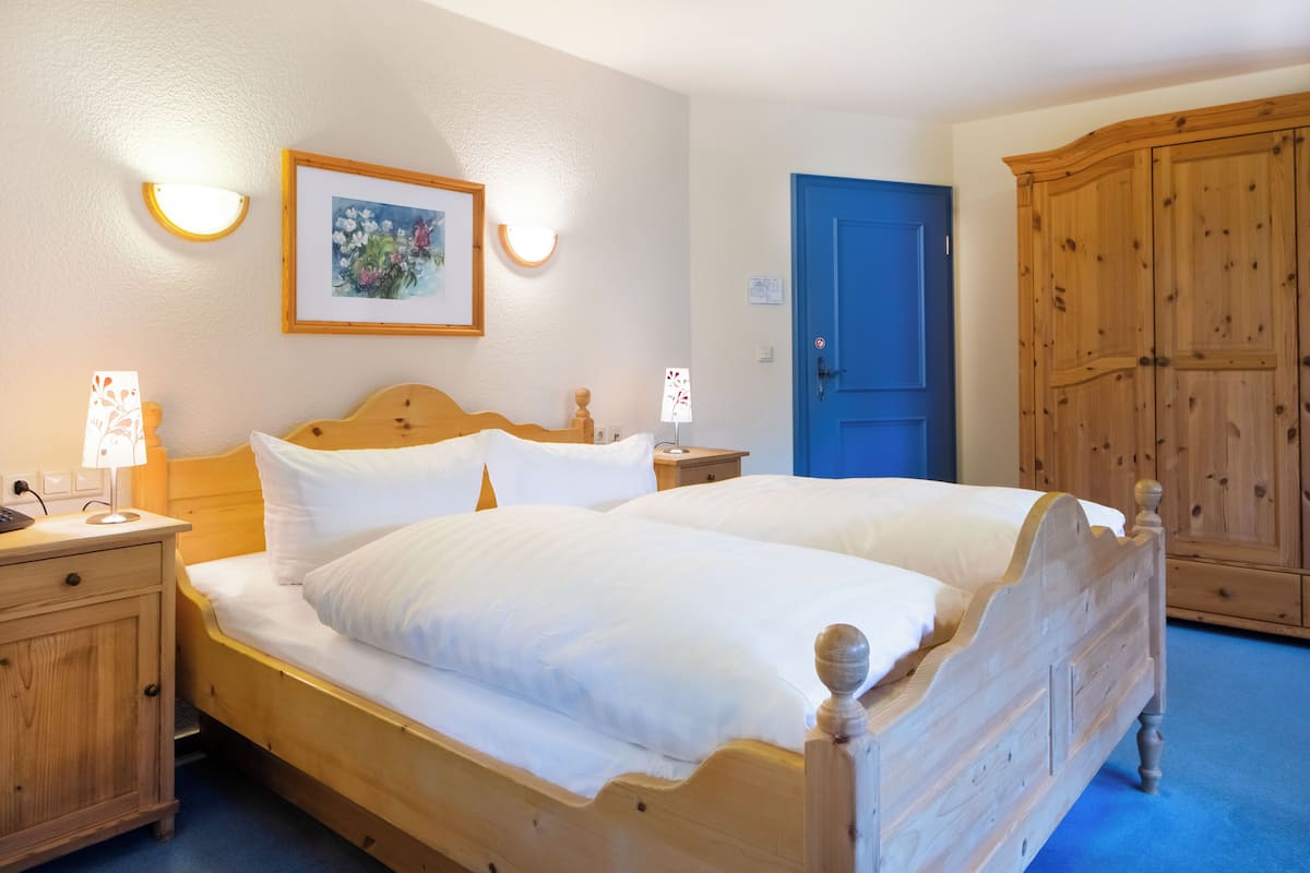 A double bed with wooden headboard, bedside lamps, a framed painting, a blue door, and a wooden wardrobe.