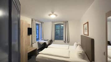 Una habitación de hotel con cama, mesita de noche, lámpara y ventana con cortinas.