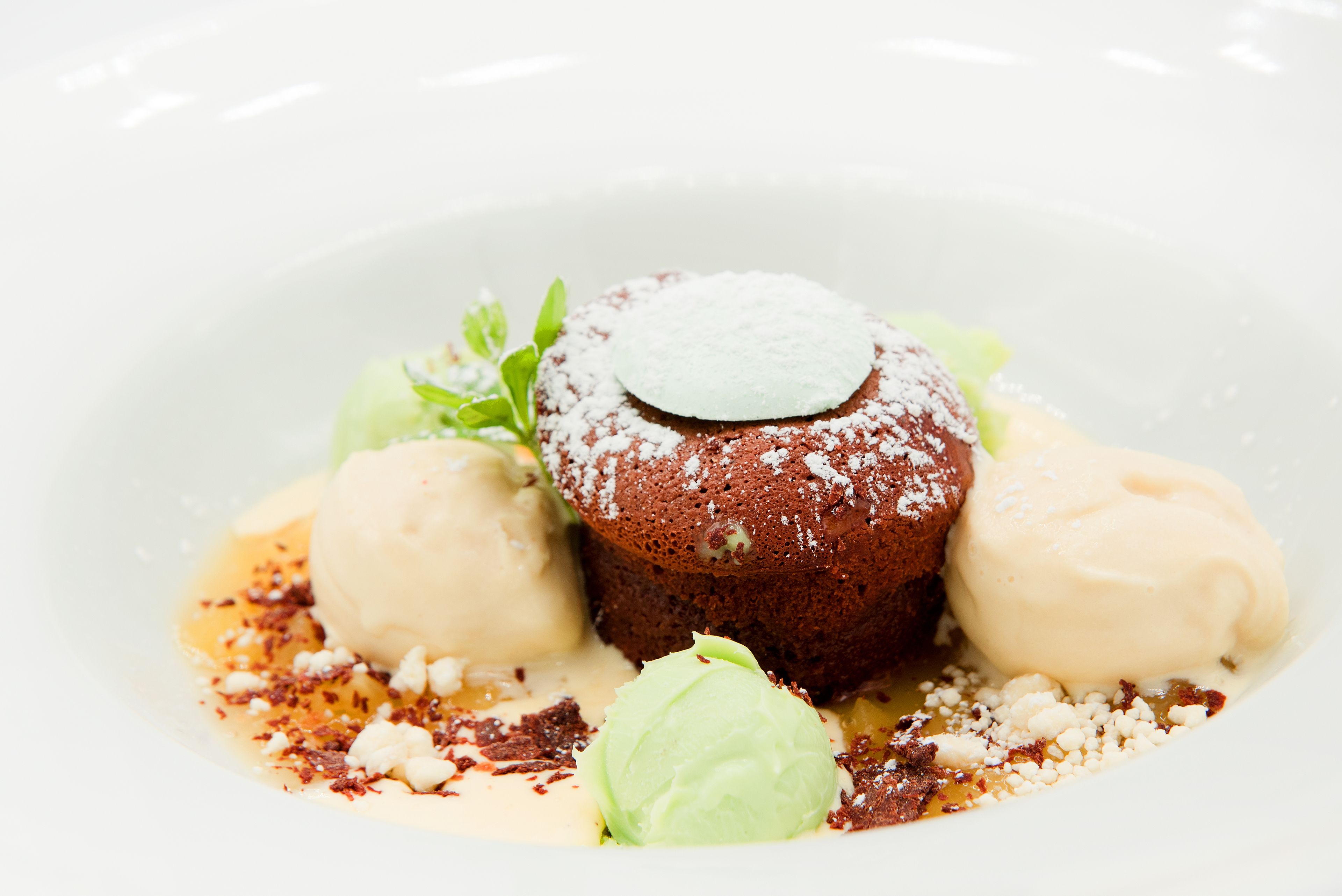 Un plato de postre con un pastel volcán de chocolate, dos bolas de helado de vainilla y un poco de azúcar glas.