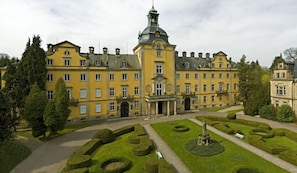 A large, yellow building with a central tower and symmetrical windows, surrounded by well-manicured gardens and trees. - Schaumburger Ritter Hotel & Restaurant (Rinteln)