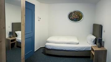 A small, compact room with a single bed, a bedside table, a lamp, and a wall-mounted picture.