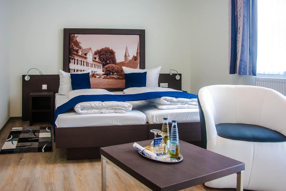 A hotel room with a bed, a chair, a table with a tray of items, and a framed picture on the wall.