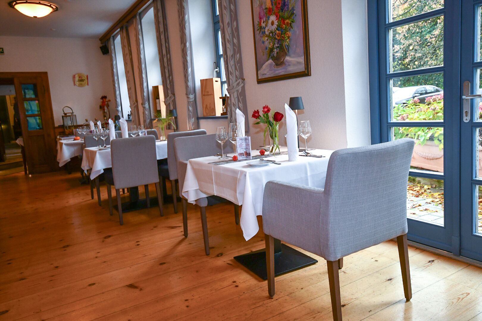 Ein Restaurant mit Holzböden, weißen Tischdecken und grauen Stühlen.