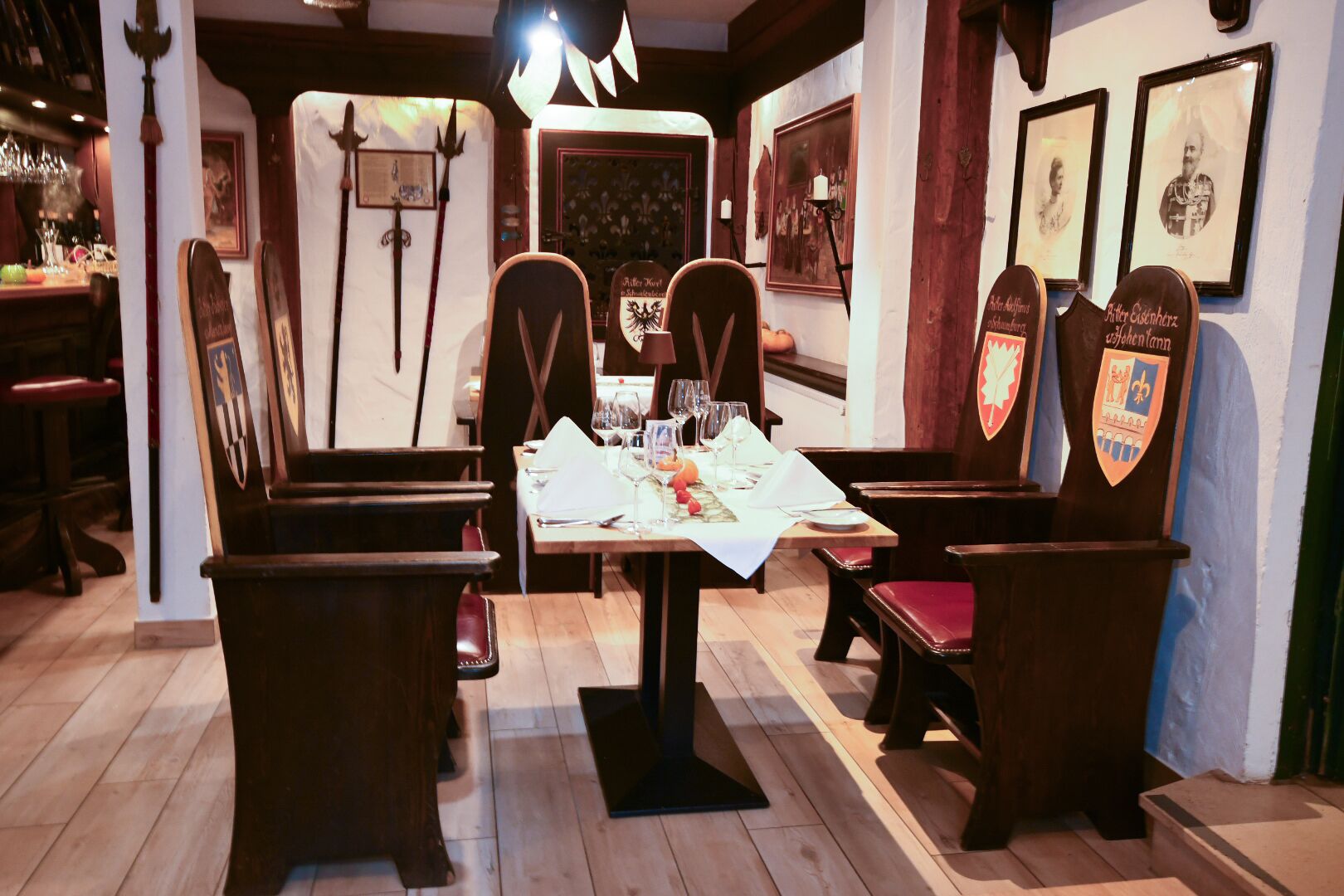 A dining area with wooden chairs and a table set for two, featuring a white tablecloth and wine glasses.