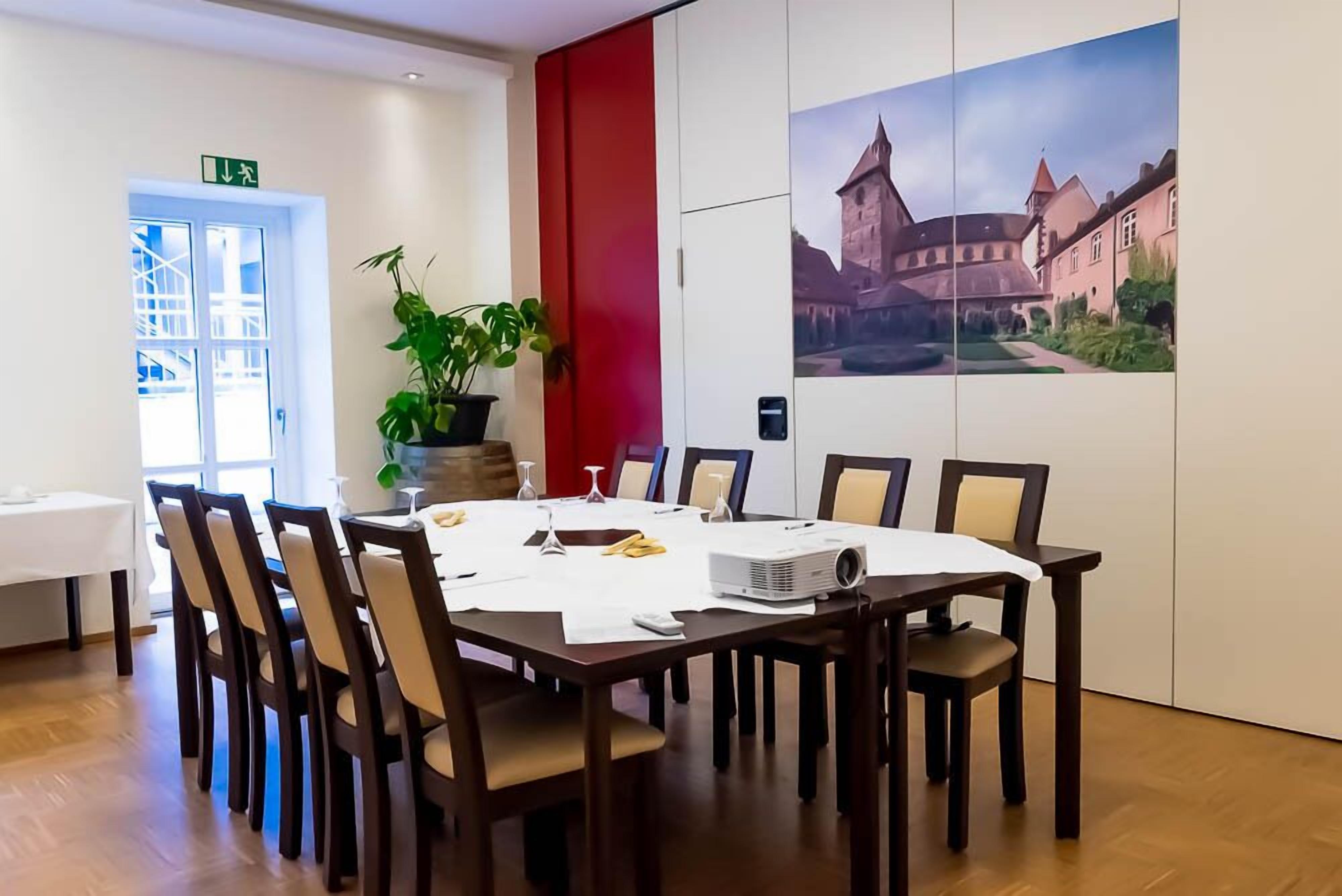 A conference room with a large table, chairs, a projector, and a potted plant.