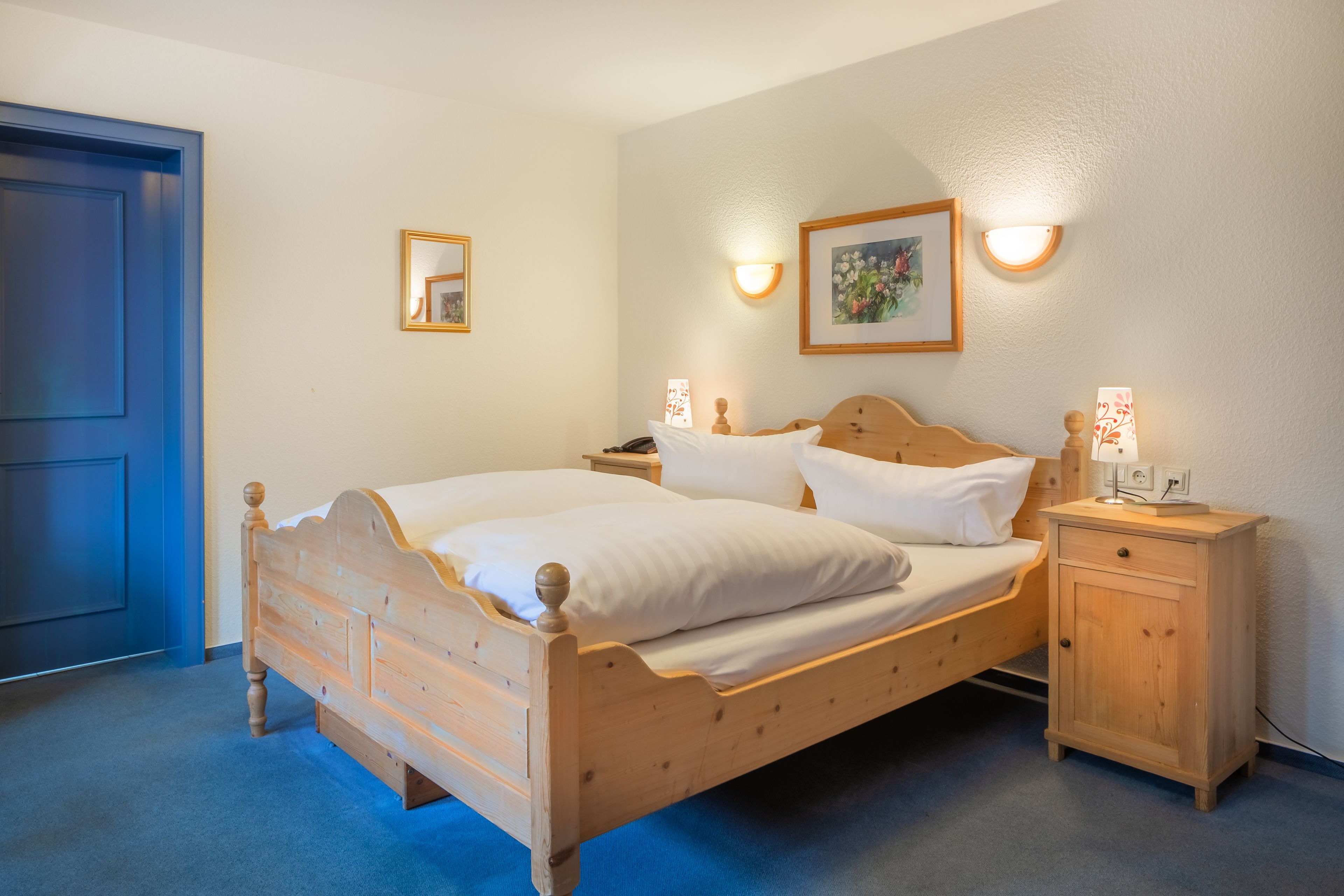 Une chambre à coucher avec un lit en bois, des tables de chevet, une commode et des lampes fixées au mur.