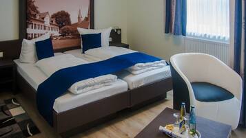 Habitación de hotel con cama, una silla, una mesa con comodidades y una ventana con cortinas.