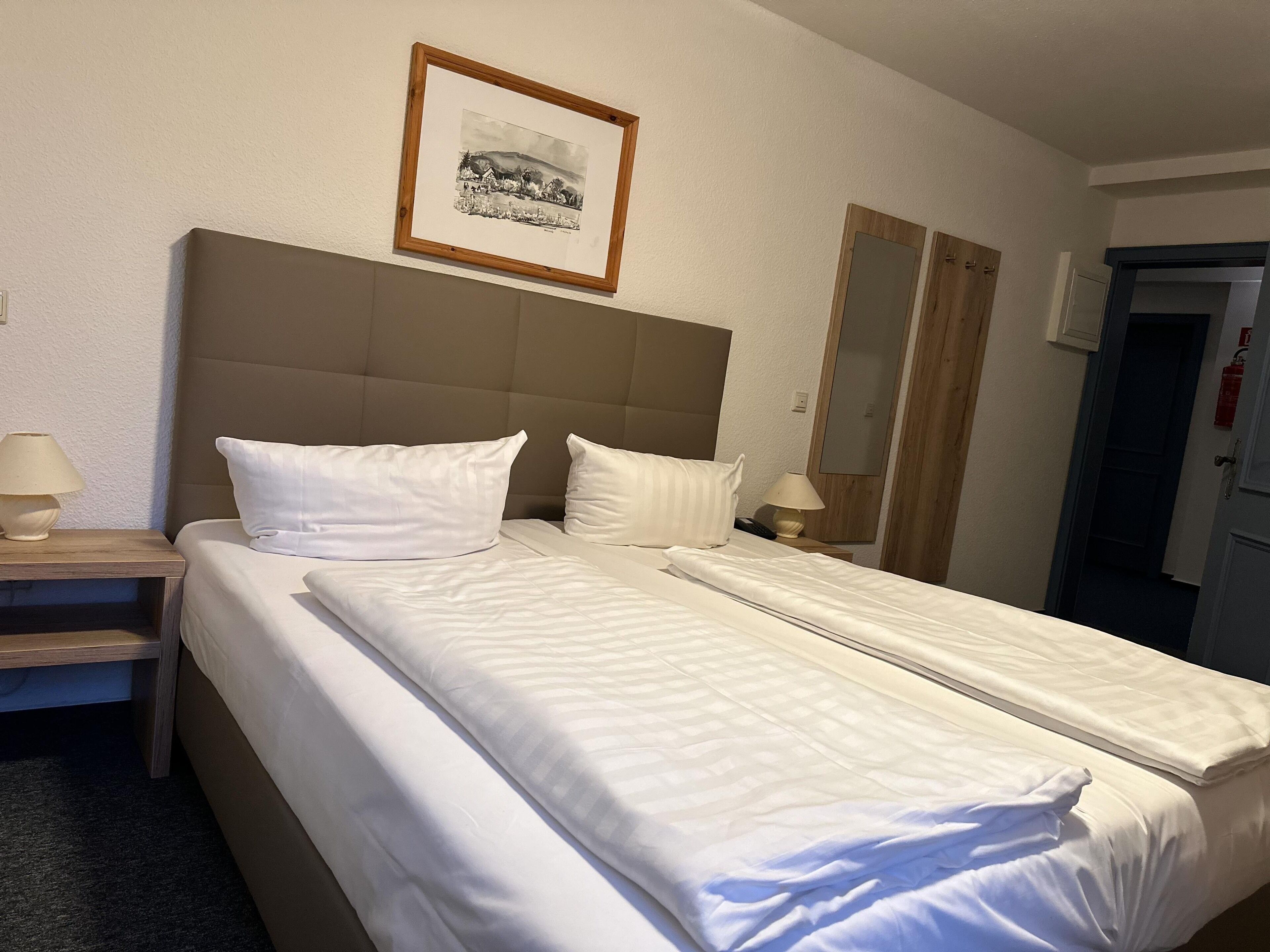 A hotel room with a large bed, two bedside tables, a framed picture on the wall, and a door to the right.