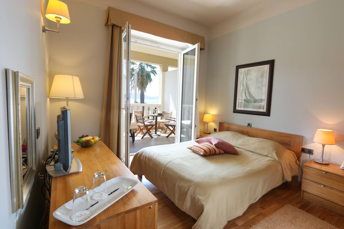 Habitación de hotel con cama, mesita de noche, lámpara y vistas al exterior.