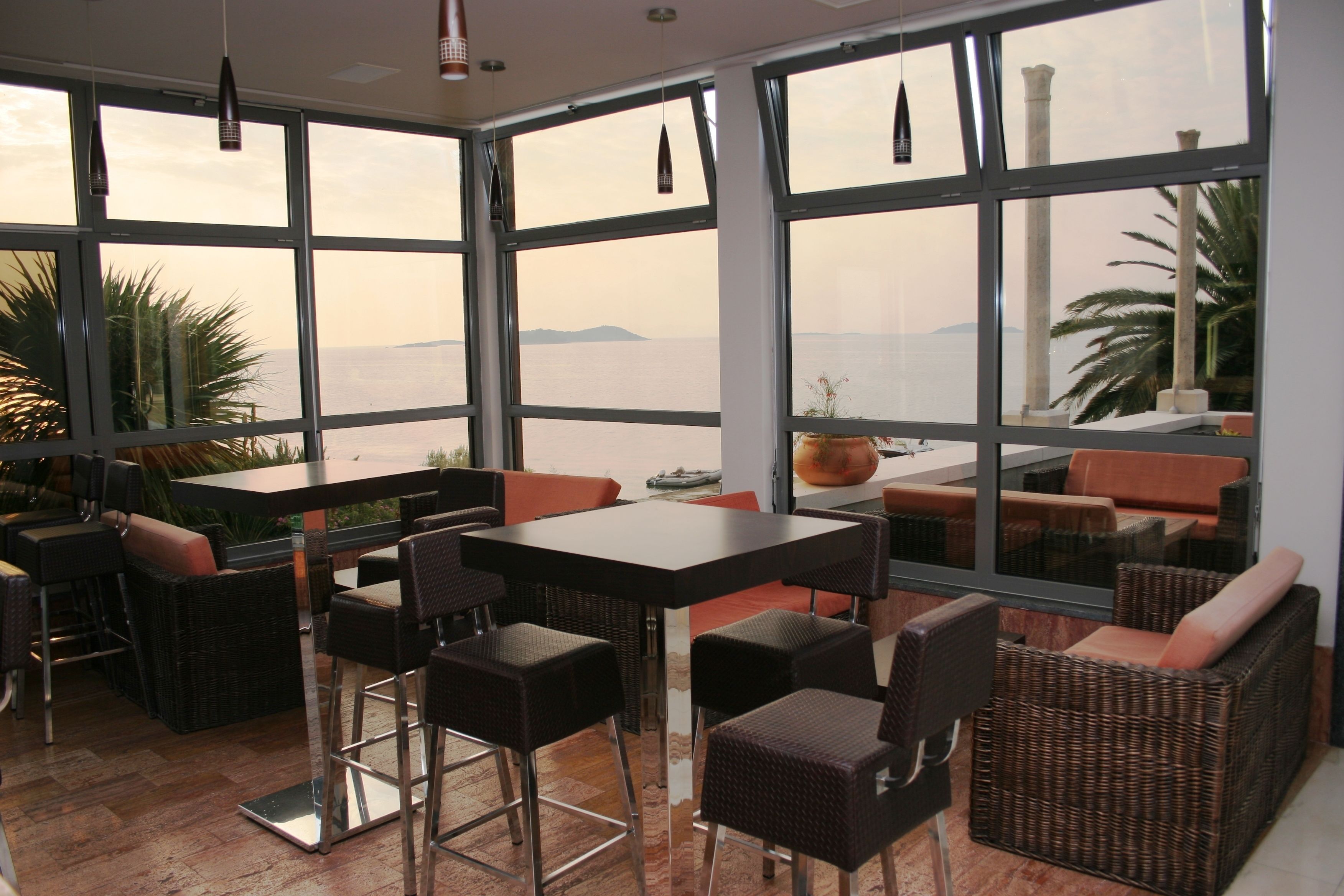 A restaurant with large windows, wicker furniture, and a view of the sea.