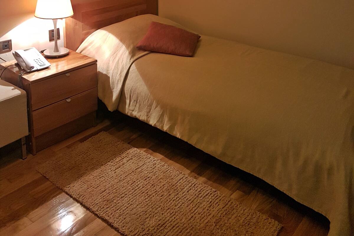 Habitación de hotel con cama, mesita de noche con lámpara, teléfono y un cuadro en la pared.