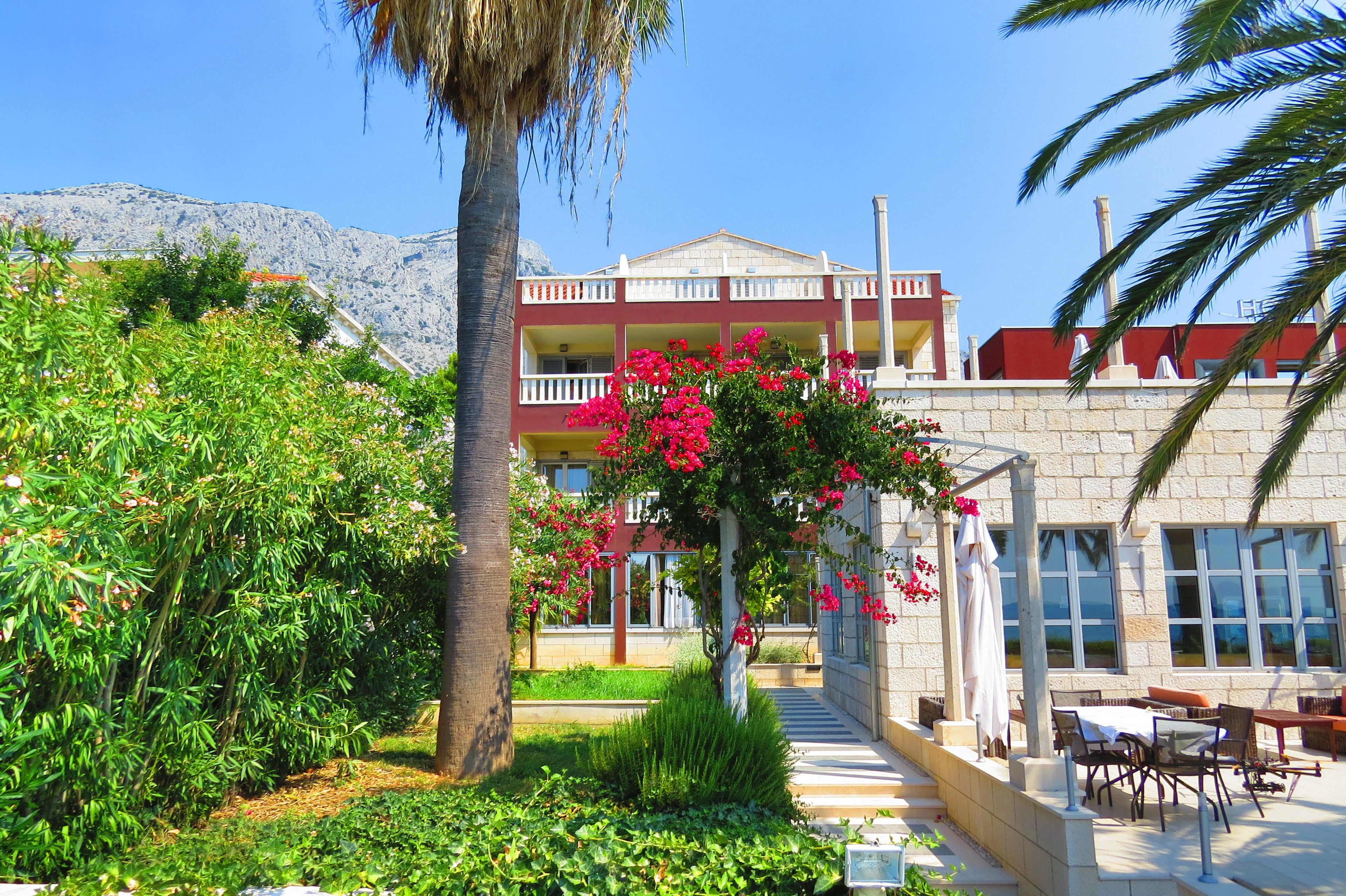 A hotel with a garden, outdoor seating, and a view of mountains.