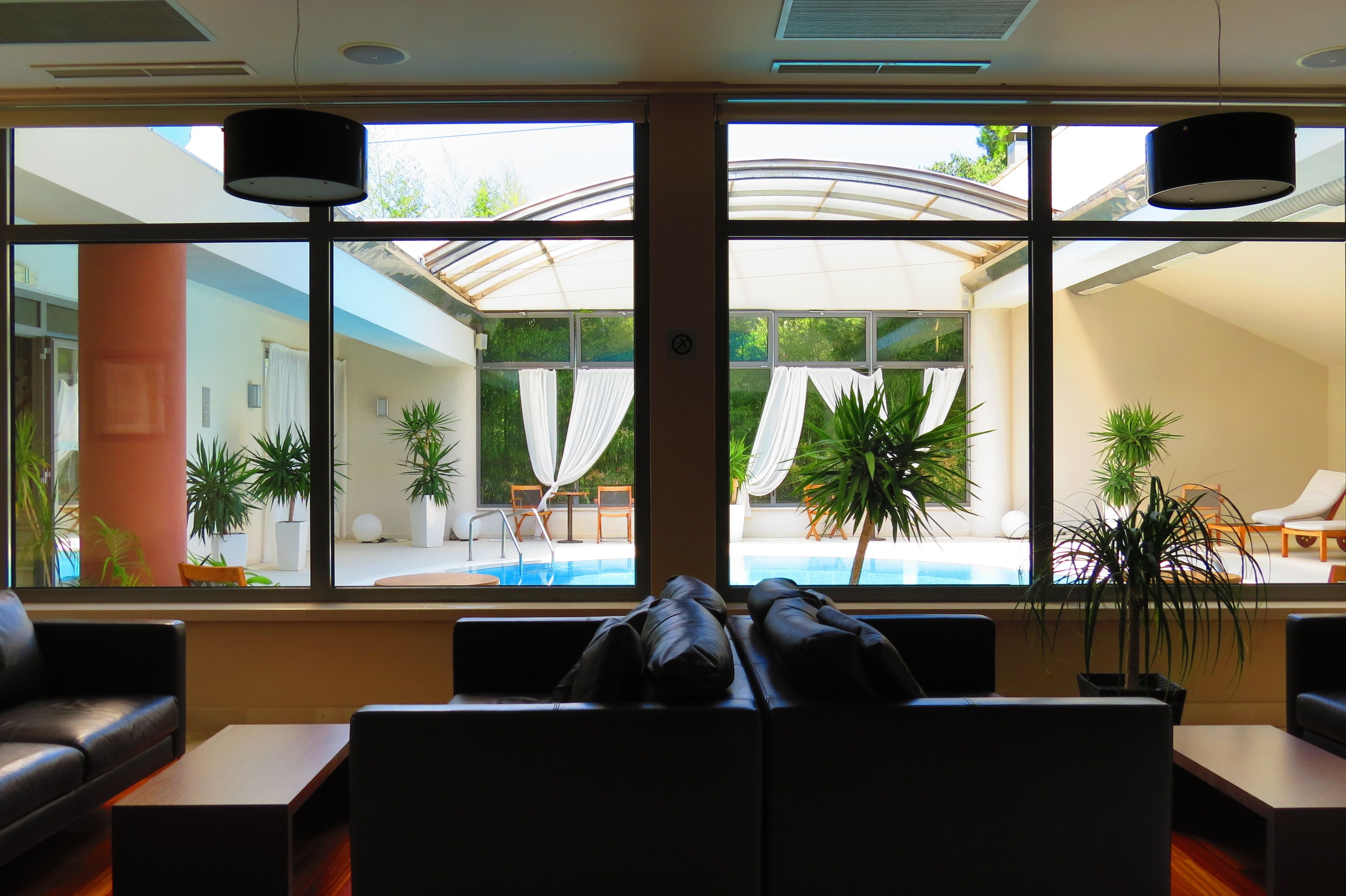 Een hotellobby met uitzicht op een zwembad, een zithoek en potplanten.