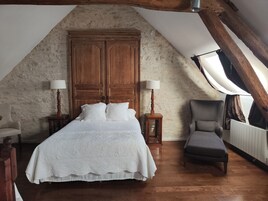 Un dormitorio con un armario grande de madera, una cama con ropa de cama blanca, dos lámparas de noche, una silla y un radiador.