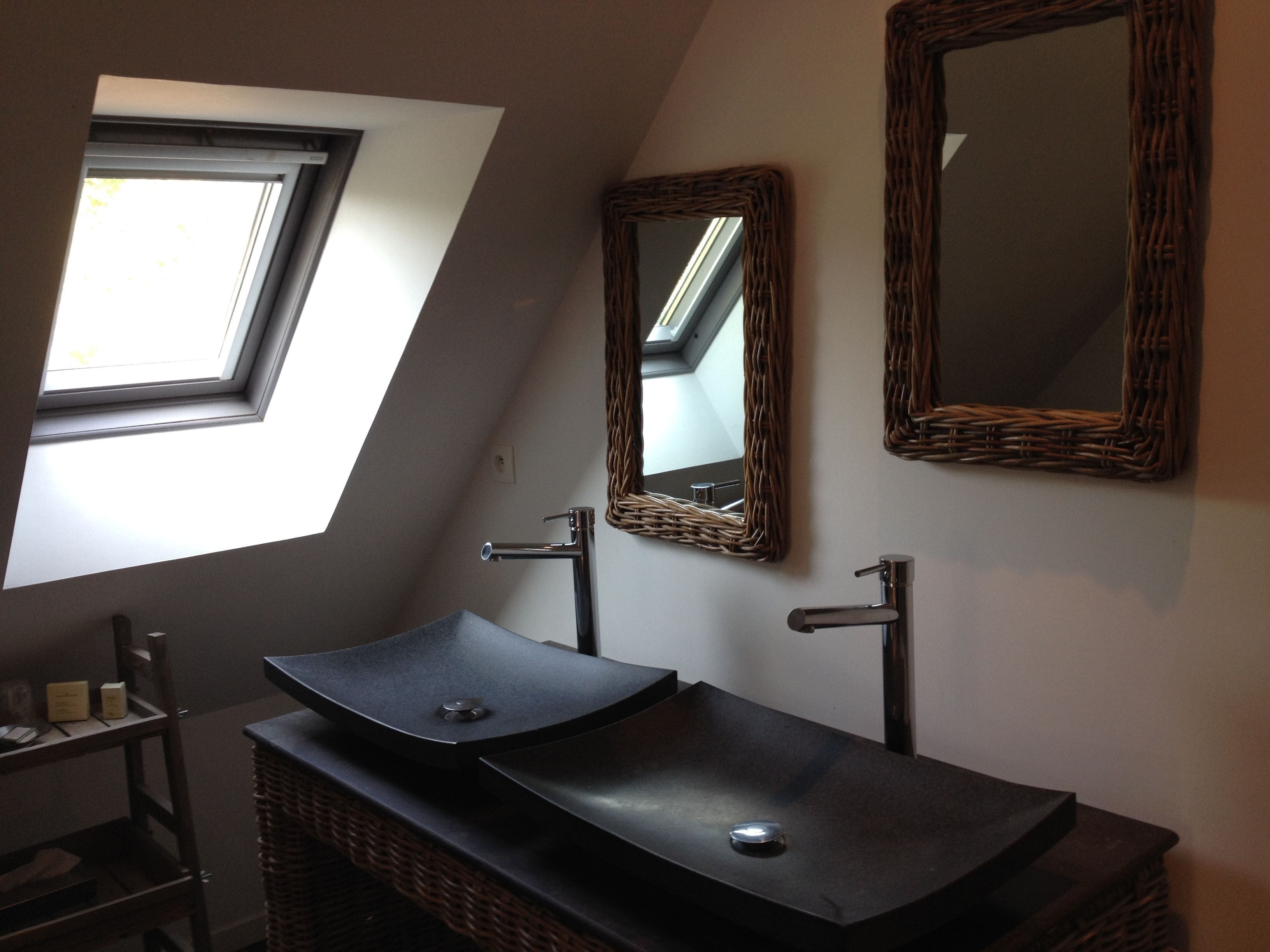 A modern bathroom with a skylight, a black vessel sink, and two mirrors with wicker frames.