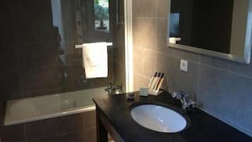 A modern bathroom with a glass-enclosed shower, a dark tiled wall, and a large mirror.