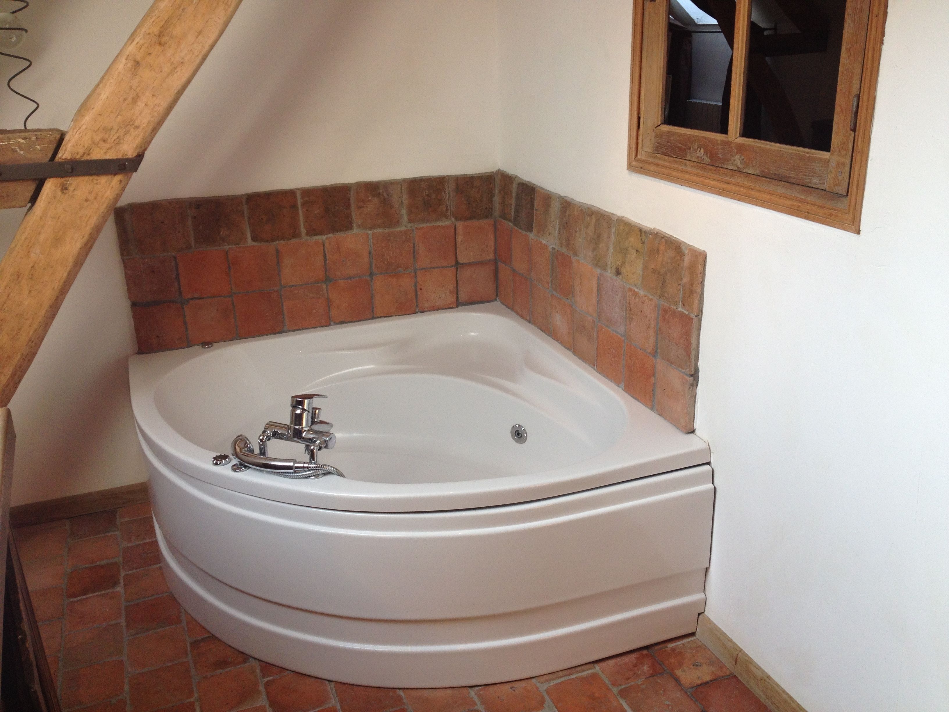 A corner bathroom with a white bathtub, a wooden staircase, and a tiled wall.