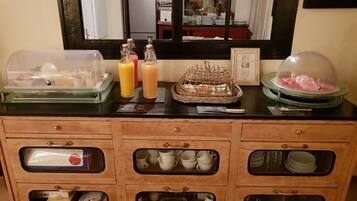 A breakfast buffet setup with a glass display case, juice bottles, and a covered food display.