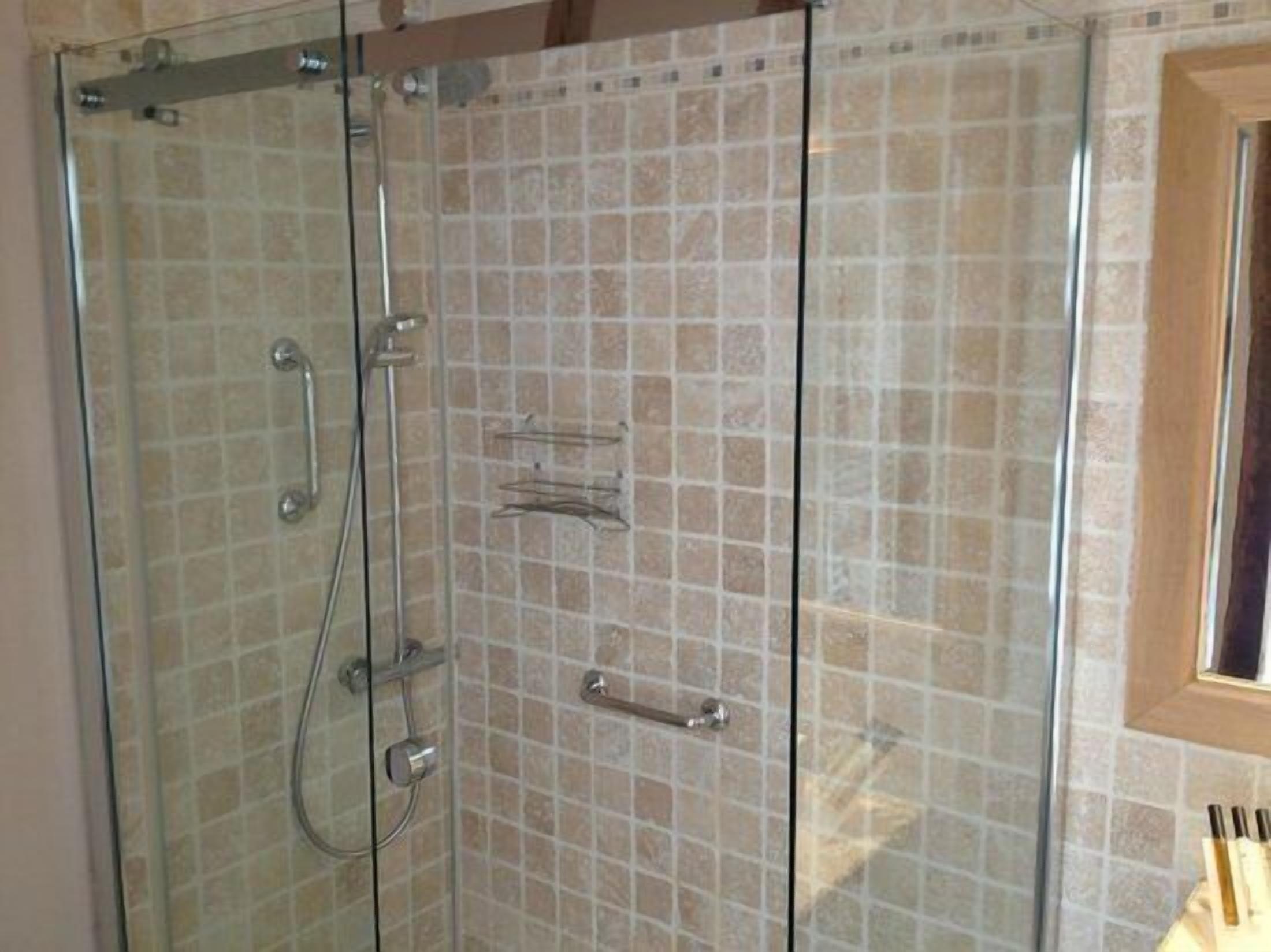 A glass-enclosed shower with tiled walls and a wooden door frame.