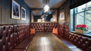 A dining area with a wooden table and brown leather booth seating, framed pictures on the wall, and a window with a view. - The Fat Badger (York)