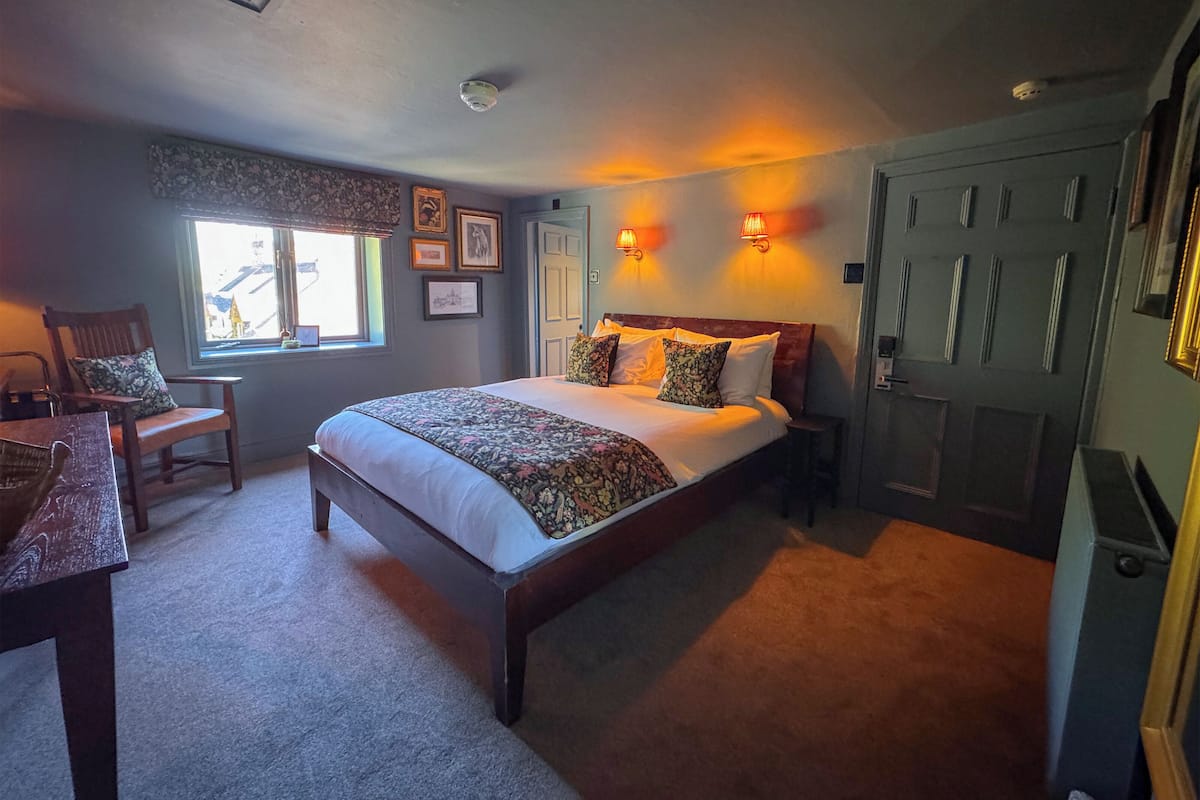 A bedroom with a large bed, a desk, a chair, a window with a view, and a door.