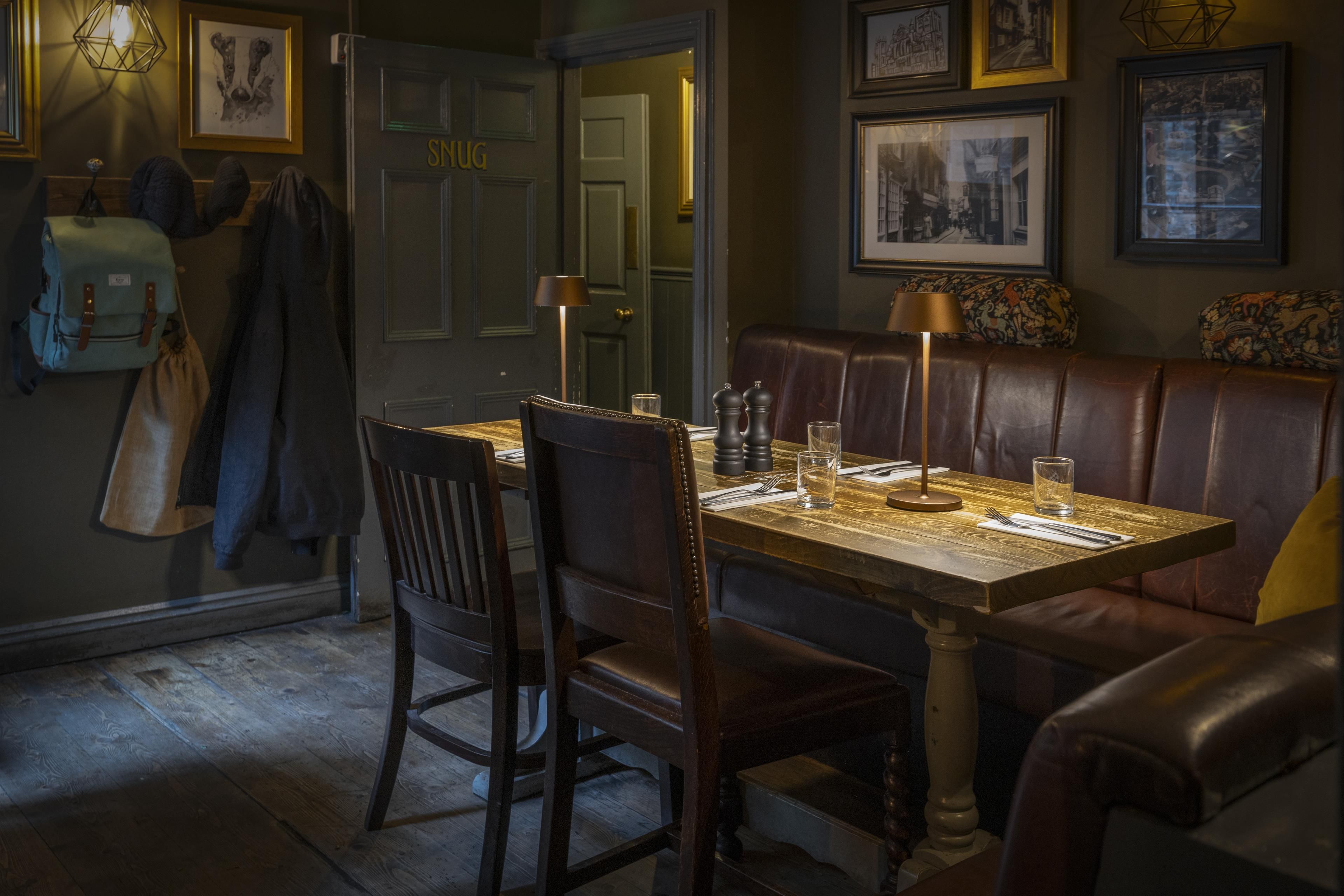 Un comedor con una mesa de madera, asientos tipo banqueta de cuero y obras de arte enmarcadas en las paredes.