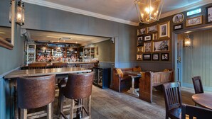 A bar area with wooden stools, a bar counter, and a seating area with benches and chairs. - The Fat Badger (York)