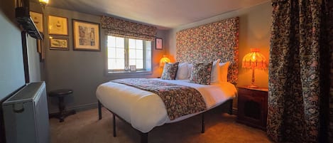 A bedroom with a large bed, two bedside lamps, a radiator, a window with a view, and patterned curtains.
