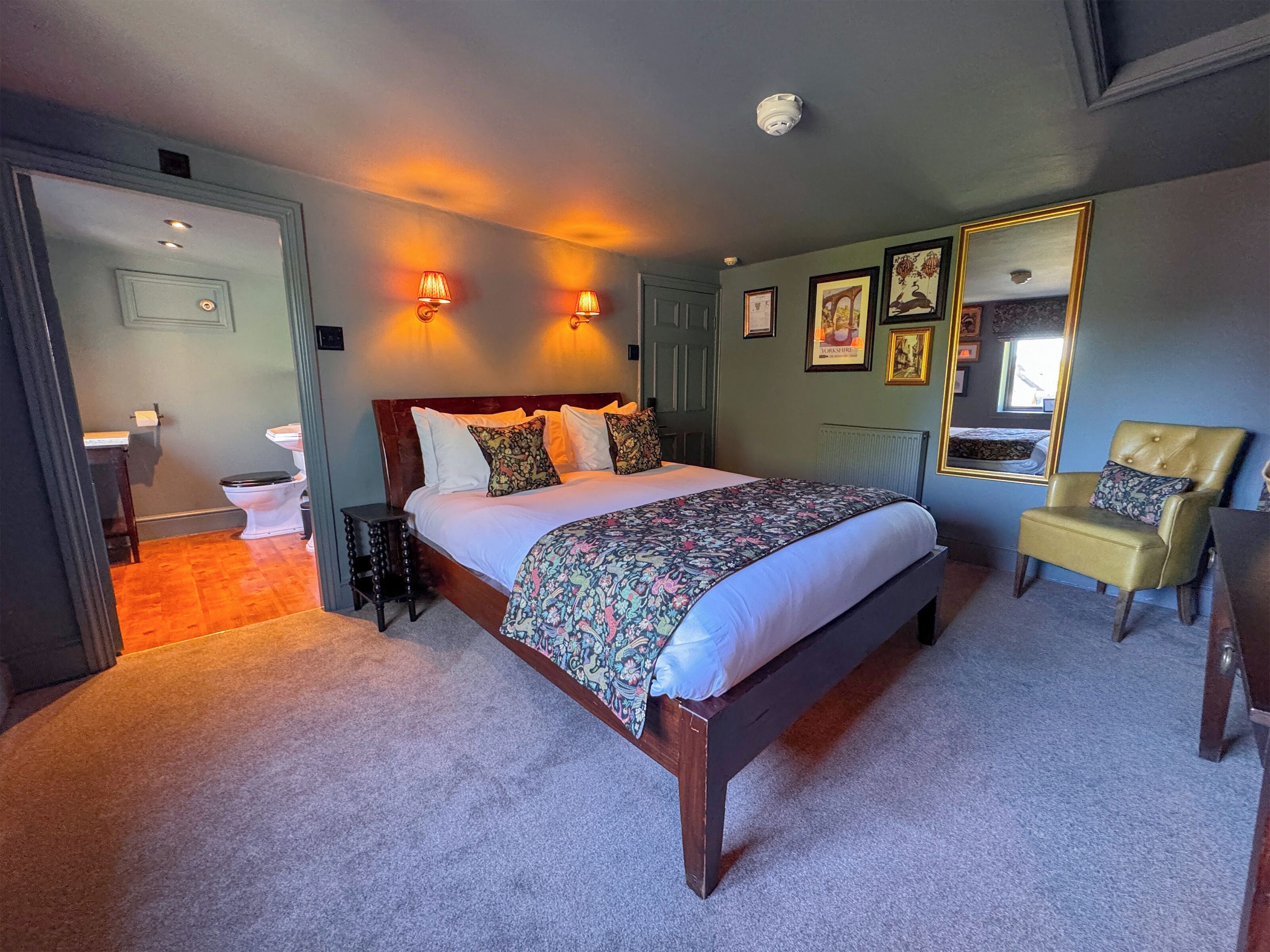 Un dormitorio con una cama grande, una silla, un espejo y un baño visible al fondo.