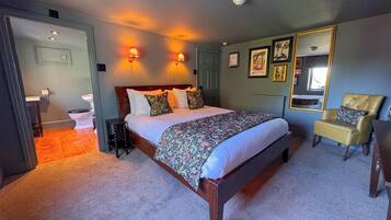 Un dormitorio con una cama grande, una silla, un espejo y un baño visible al fondo.